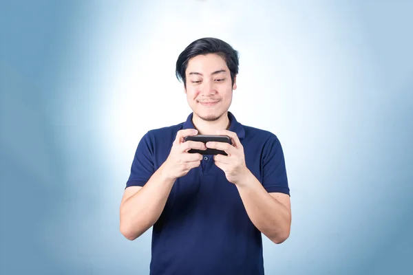 Chico asiático con teléfono móvil en la mano, sobre fondo azul — Foto de Stock