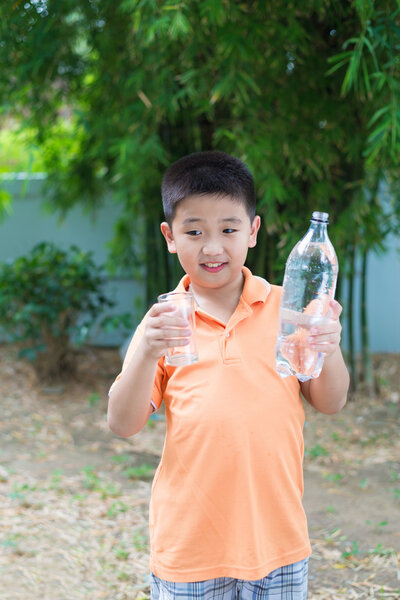 Азиатский мальчик наливает воду в стекло из бутылки
,