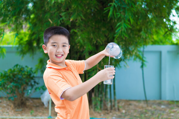 Азиатский мальчик наливает воду в стекло из бутылки
,