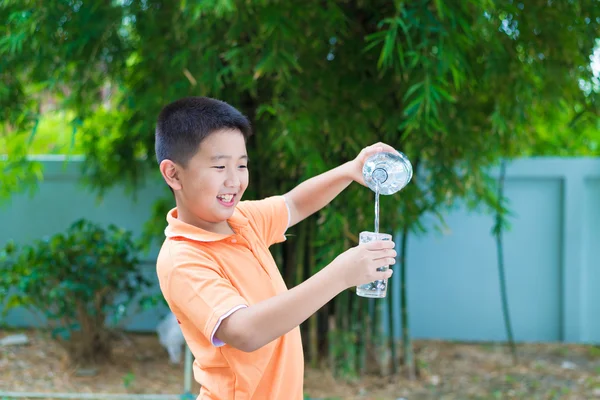 Asiatiska boy hälla vatten i glas från flaska, — Stockfoto