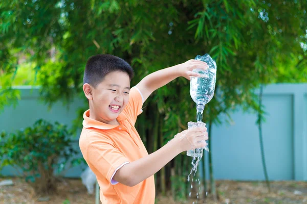 Asiatiska boy hälla vatten i glas från flaska, — Stockfoto