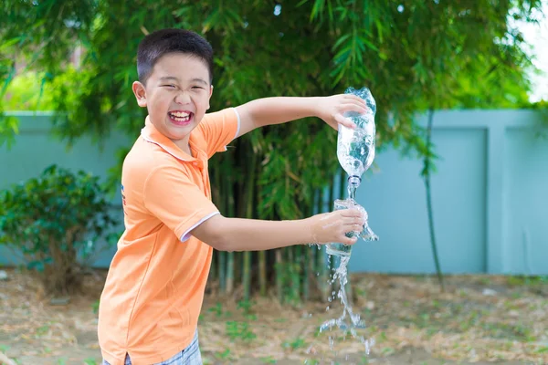 Asiatischer Junge gießt Wasser aus Flasche ins Glas, — Stockfoto