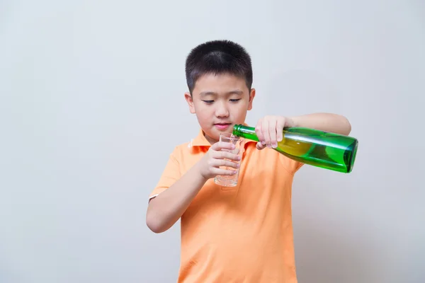 Asiatico ragazzo versando acqua in vetro da un verde bottiglia , — Foto Stock