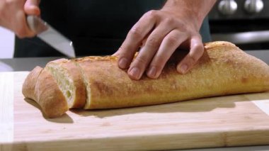 Şef ekmeği ağır çekimde kesiyor, ekmeği ahşap kesme tahtasıyla dilimliyor, ekmeği yakın plan doğruyor.