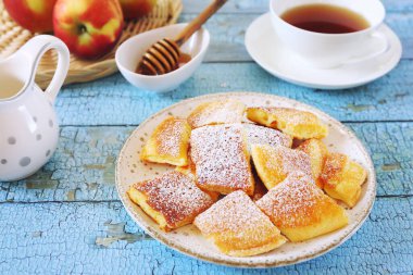 Avusturya mutfağı. Yırtık krep (veya omlet) bal ile kaiserschmarrn, pudra şekeri sosu ve mavi arkaplanda tatlı kahvaltı için bir fincan çay