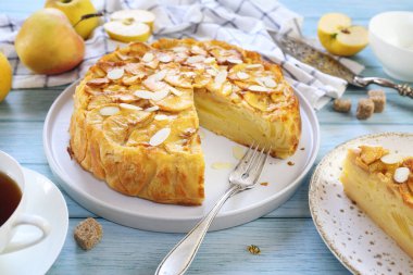 Fransız mutfağı. Görünmez elmalı tart, badem yaprağı sosu, sarı elma ve mavi arkaplanda bir fincan çay.