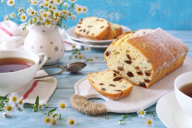 Yaz tatlısı. Yunan yoğurdu, kuru üzümlü kek ve mavi arka planda iki fincan çay. 