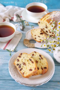 Yaz tatlısı. Yunan yoğurdu, kuru üzümlü kek ve mavi arka planda iki fincan çay. 