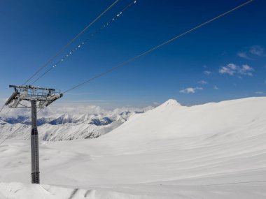 Gürcistan 'ın Gudauri kentinde açık bir kış gökyüzü altında el değmemiş karla kaplı dağlara karşı modern bir kayak kaldırma direğinin panoramik görüntüsü. Kış sporları ve seyahat temaları için ideal.