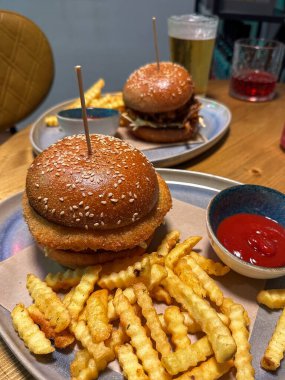 İki lezzetli burger, kıtır kıtır patates kızartması ve ketçap ile sıradan bir restoran ortamında kırsal ahşap bir masada, doyurucu bir yemek için mükemmel..