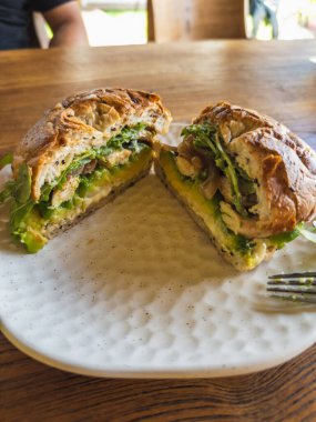 Lezzetli ve sağlıklı bir tavuk ve avokado sandviçi, taze ikiye bölünmüş, beyaz desenli bir tabakta canlı içerik katmanları ortaya çıkarıyor, gurme bir öğle yemeği için mükemmel..