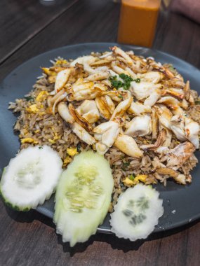 Lezzetli Tayland yengeci. Koyu bir tabakta servis edilmiş. Köy ahşap bir masada salatalık dilimleri var. Arka planda ferahlatıcı bir buzlu çay bulanıklaşıyor ve özgün bir Güneydoğu Asya çayı yaratıyor.