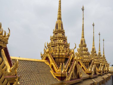 Bangkok, Tayland 'daki görkemli altın kuleler ve Loha Prasat, Wat Ratchanatdaram' ın çok katmanlı çatıları. Yumuşak, bulutlu bir ışık altında karmaşık Budist tapınak mimarisi.