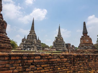 Tayland 'daki Ayutthaya Tarih Parkı' nın ruhani ihtişamına dalın. Antik stupalar ve tapınak kalıntıları, tarihsel mirası zengin, parlak bir gökyüzü altında, yıpranmış tarafından çerçevelenmiş, görkemli bir şekilde yükselir