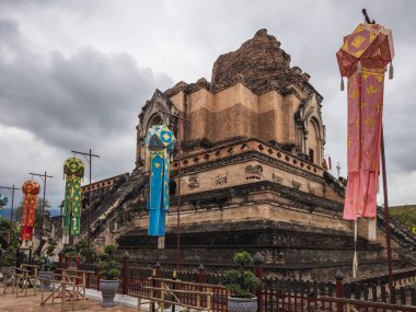 Chiang Mai, Tayland 'daki Antik Wat Chedi Luang, görkemli bir şekilde bulutlu bir gökyüzünün altında duruyor, canlı geleneksel Lanna fenerleriyle süslenmiş, zengin kültürel mirası sergiliyor..