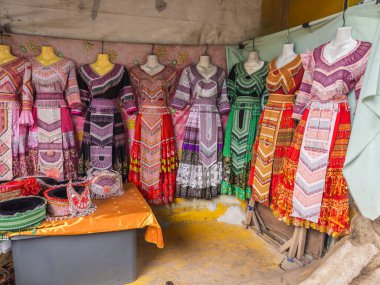 Hareketli bir pazar yerinde mankenler üzerinde geleneksel Hmong etnik giysilerinin canlı bir şekilde sergilenmesi, karmaşık nakışlar, renkli desenler ve kültürel miras sergilenmesi.