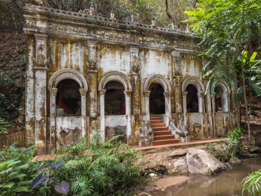 Chiang Mai, Tayland 'daki Wat Umong' daki antik Budist tapınağı harabeleri, sakin bir nehir önü ile yemyeşil tropikal ormanların arasına yerleşmiştir. Tarihi ve ruhani bir geri çekilme.