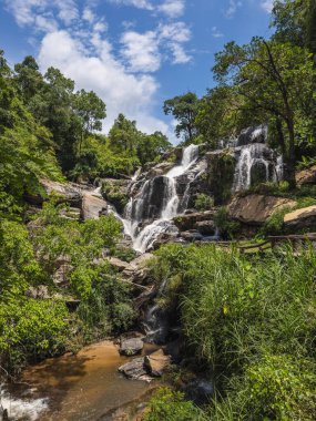 Majestic Mae Ya Şelalesi, açık ve bulutlu bir alan altında, Tayland 'daki Doi Inthanon Ulusal Parkı' ndaki verimli tropikal ormanların ortasında kayalıklardan zarifçe süzülüyor. Huzurlu bir doğa harikası...