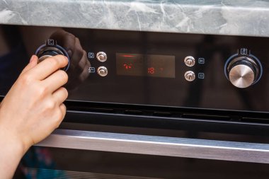 Evde pasta yapmak için dişi el fırını açıyor. Fırın topuzuna yakın çekim. Siyah elektrikli fırının manzarası, sıcak hava ikonu olan düğme. Yemek ısıtma, kek pişirme kavramı..