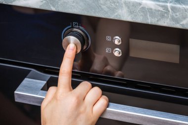 Evde pasta yapmak için dişi el fırını açıyor. Fırın topuzuna yakın çekim. Siyah elektrikli fırının manzarası, sıcak hava ikonu olan düğme. Yemek ısıtma, kek pişirme kavramı..