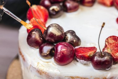 Siyah eldivenli kadın eli, hindistancevizli cheesecake 'in üstüne çilek ve kirazların üzerine yenebilir altın koyar..