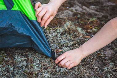 Güzel kız çadır kuruyor. Çadırı yere çivilemek için metal çubuklar kullanıyor. Kamp ve açık hava konsepti.