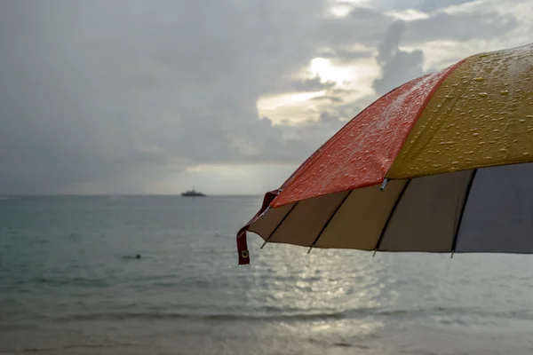 Ombrello colorato sotto la pioggia e sfondo spiaggia sfocata — Foto Stock