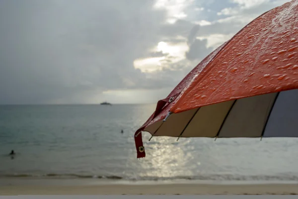 Ombrellone sotto la pioggia e sfondo spiaggia sfocata — Foto Stock