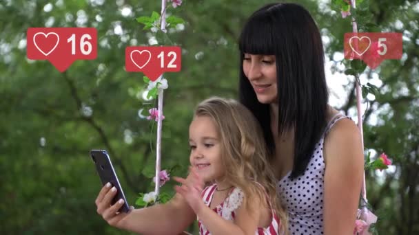 Krásná mladá roztomilá dívka s dítětem interaguje s chytrým telefonem, napíše text na obrazovce telefonu, ikony sociální sítě se stejným počtem účastníků rychle zvýšit — Stock video