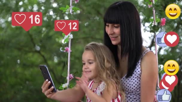 Une belle jeune fille mignonne avec un enfant interagit avec un smartphone, tape du texte sur l'écran du téléphone, les icônes des réseaux sociaux avec le même nombre d'abonnés augmentent rapidement dans — Video