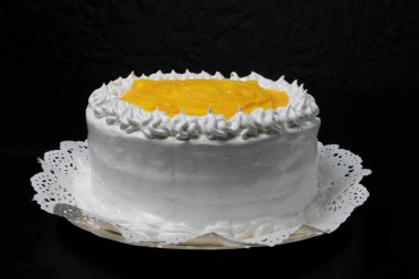 Ortasında beyaz krema ve meyve olan siyah arkaplan olan bir pastaya yüksek açılı yakın plan.