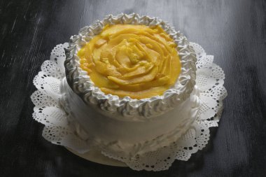 Ortasında beyaz krema ve meyve olan siyah arkaplan olan bir pastaya yüksek açılı yakın plan.