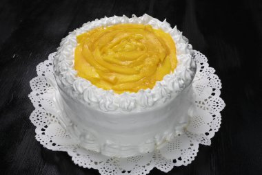 Ortasında beyaz krema ve meyve olan siyah arkaplan olan bir pastaya yüksek açılı yakın plan.