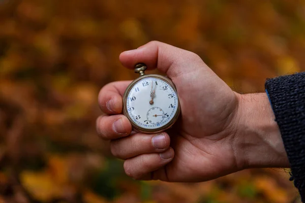 Vintage Pocket watch in man\'s hand against the background of autumn dried brown leaves