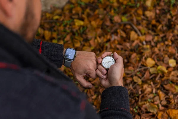Vintage Pocket watch in man\'s hand and smart watch on the wrist against the background of autumn dried brown leaves