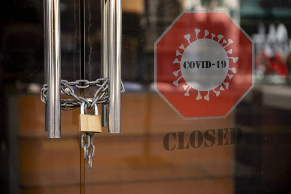 Closed Store due to Coronavirus pandemic. Locked Store Door with Padlock and Chains and Covid 19 sign