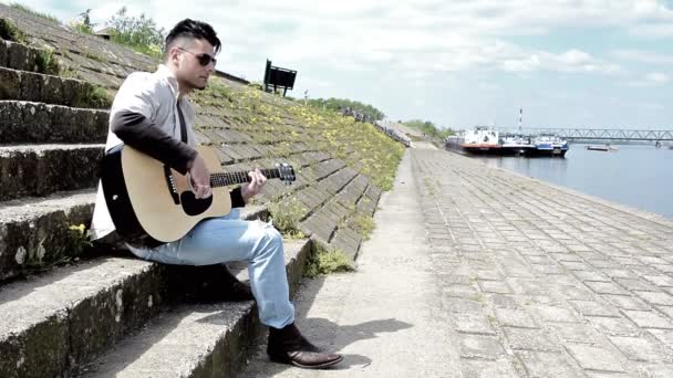 Man acustic gitaar spelen naast de rivier — Stockvideo