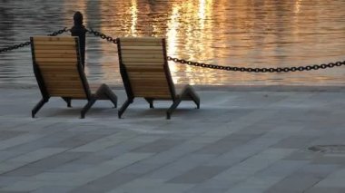 Gün batımında suda. Alacakaranlıkta iskelede iki sandalye ışıldayan bir altın dalgaya karşı. Güverte sandalyesi.