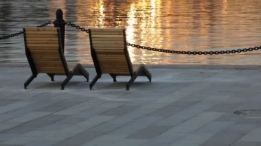 Gün batımında suda. Alacakaranlıkta iskelede iki sandalye ışıldayan bir altın dalgaya karşı. Güverte sandalyesi.