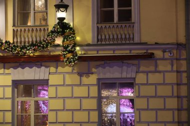 Noel ağacı dalları ve yanan ışıklarla duvarda asılı Noel toplarıyla binanın ön cephesinde parlayan tatil ışığı camları. Gözlükler havai fişekleri yansıtıyor.