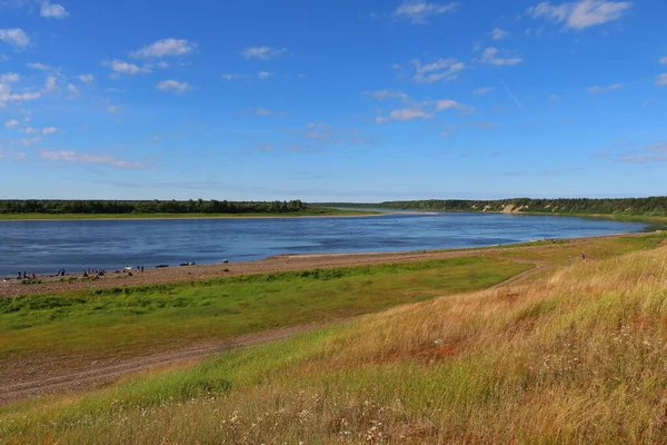 Sahilden açık alanlara geniş ve uzun nehirli panoramik görüntüler, çayırlar ve güneşli bir günde denize yakın tekneleri olan turistler. Mavi bir gökyüzü.