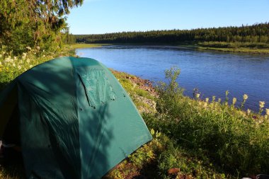 Güzel bir gölün güneşli sahilinde kapalı pencereli, turist yeşil çadırının görüntüsü. Sakin bir su, mavi gökyüzü ve ufukta bir yaz sabahı ormanı.