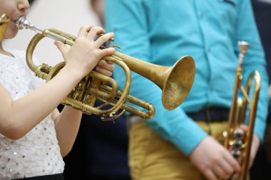 Küçük bir müzisyen kız ellerinde pullarla beyaz bir bluz tutuyor ve eski bir trompette bir melodi çalıyor. Mavi gömlekli bir öğretmene bir ders veriyor.