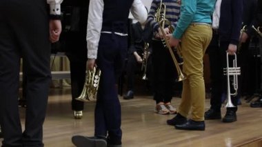 Okul çocuklarından oluşan bir grup müzik aletli genç müzisyen derslerdeki parke üzerinde duruyorlar. Bir çocuk komik bir şekilde ayak basıyor. Okul müzik eğitimi kavramı.