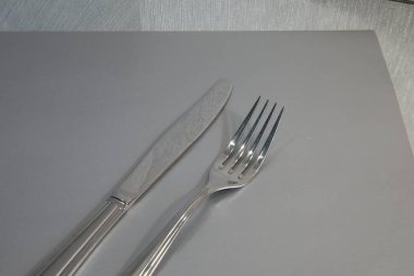 Gri bir peçetenin üzerinde bir çatal ve bıçak servis edilir. Tek renkli görüntü. Gri arkaplan. Günlük hayatın gümüş çatal bıçak seti.