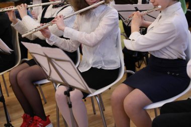 Bayan öğrenciler okul orkestrasındaki bir sınıfta gümüş flüt ve siyah etek ile müzik aleti çalıyorlar. Müzik öğretmenliği konsepti. Grup eğitimi.