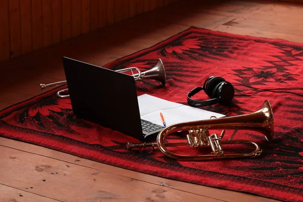 Musical attributes.Laptop headphones sheet music with a pencil two wind musical instruments on a wooden floor with a red blanket.Set of the musician of the creative person.Work and leisure concept