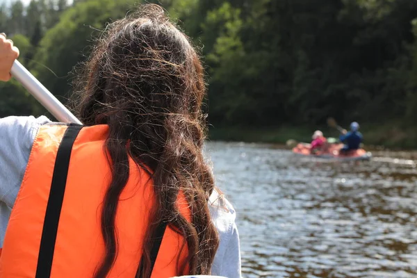 Young woman in a boat.Portrait of a brunette girl with a paddle on a canoe in protective equipment on the water in an orange vest back view close-up.Water sports concept.Outdoor activity background