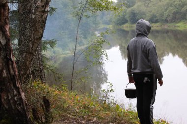 Suyun kenarındaki ormanda yürüyorum. Spor giysili bir kapüşonlu ve sabahın erken saatlerinde Rusya 'nın sisli manzarasında göl kenarında yürüyüş şapkalı bir adam. Turist tatili kavramı.