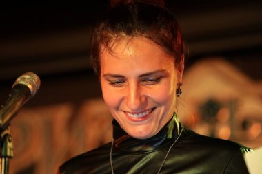 Bir mikrofon şarkıcısının portresi. Siyah, mutlu, esmer bir kadın. Yakından gülümsüyor.